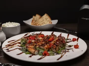 Grilled octopus with tomatoes, arugula, and balsamic glaze on a white plate.