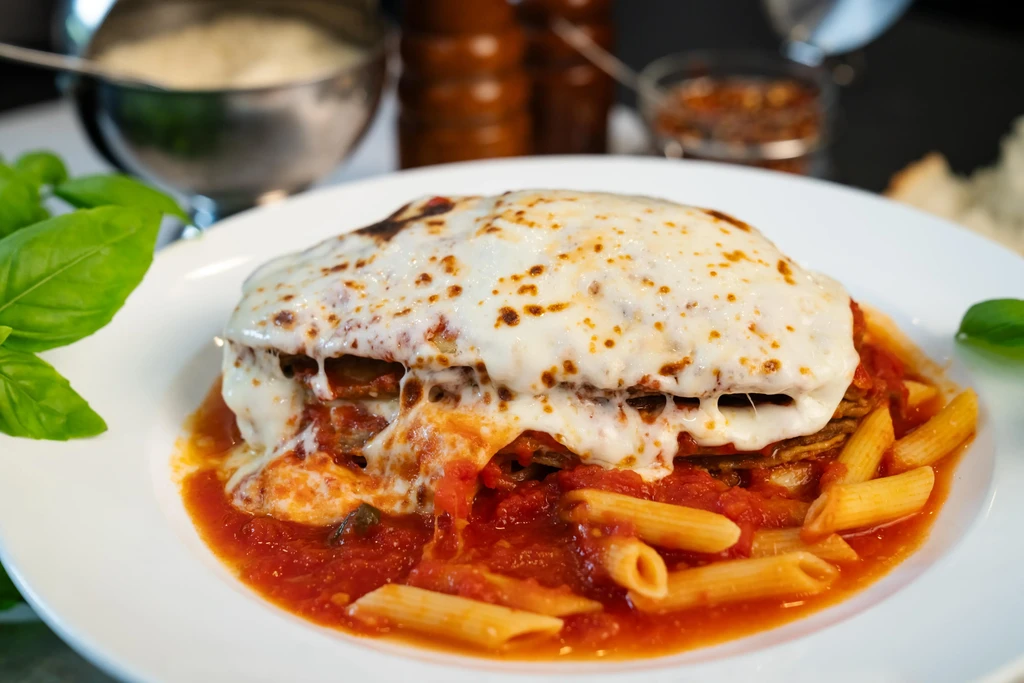 Eggplant parmesan covered in melted cheese, served with penne pasta in red sauce.