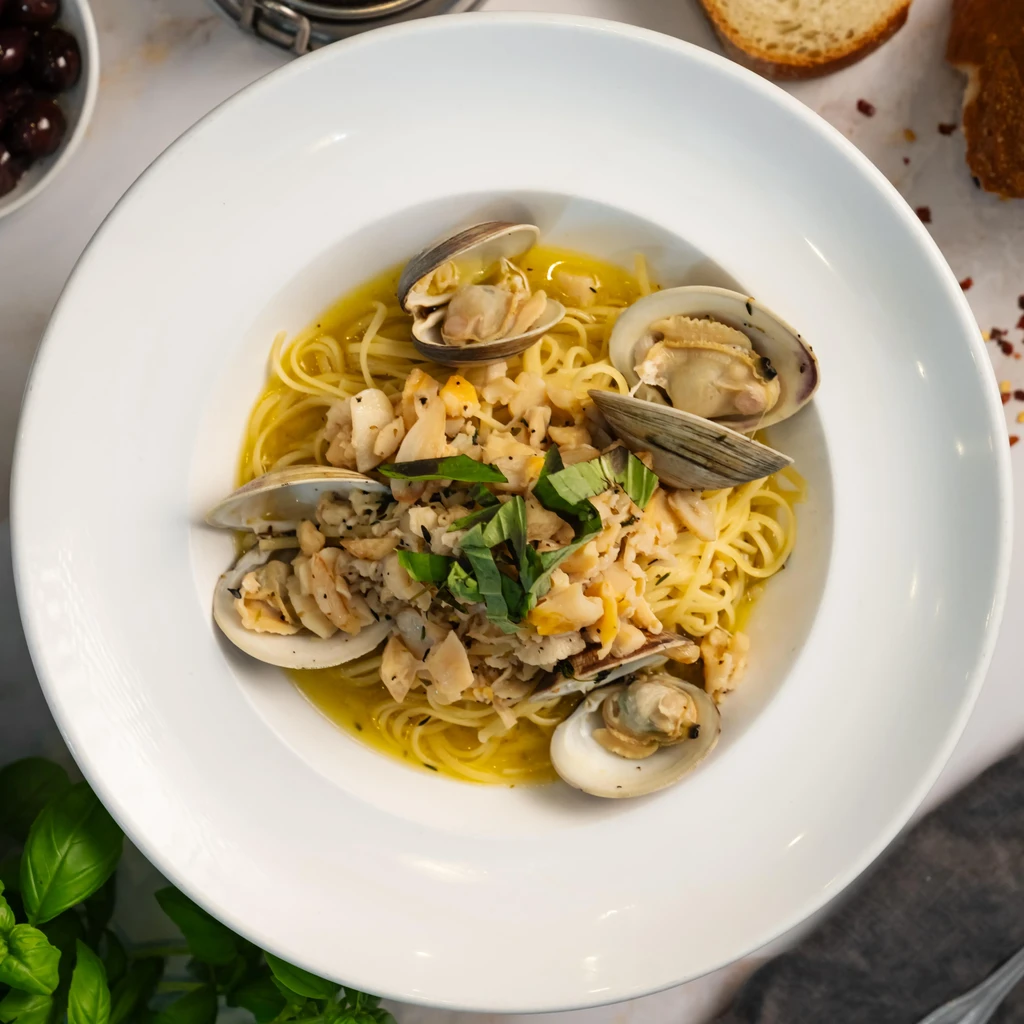 Spaghetti with clams in a white bowl with fresh basil.