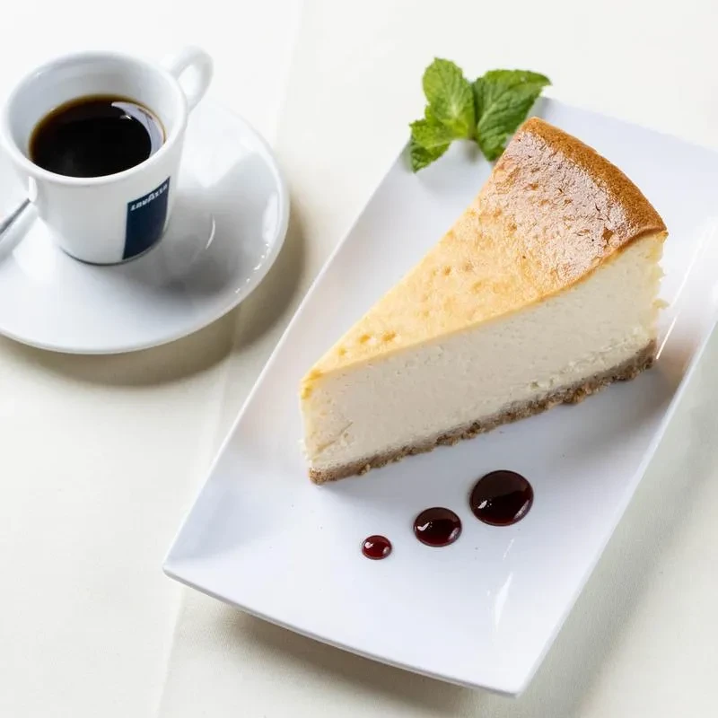 A slice of cheesecake with espresso on a white table.