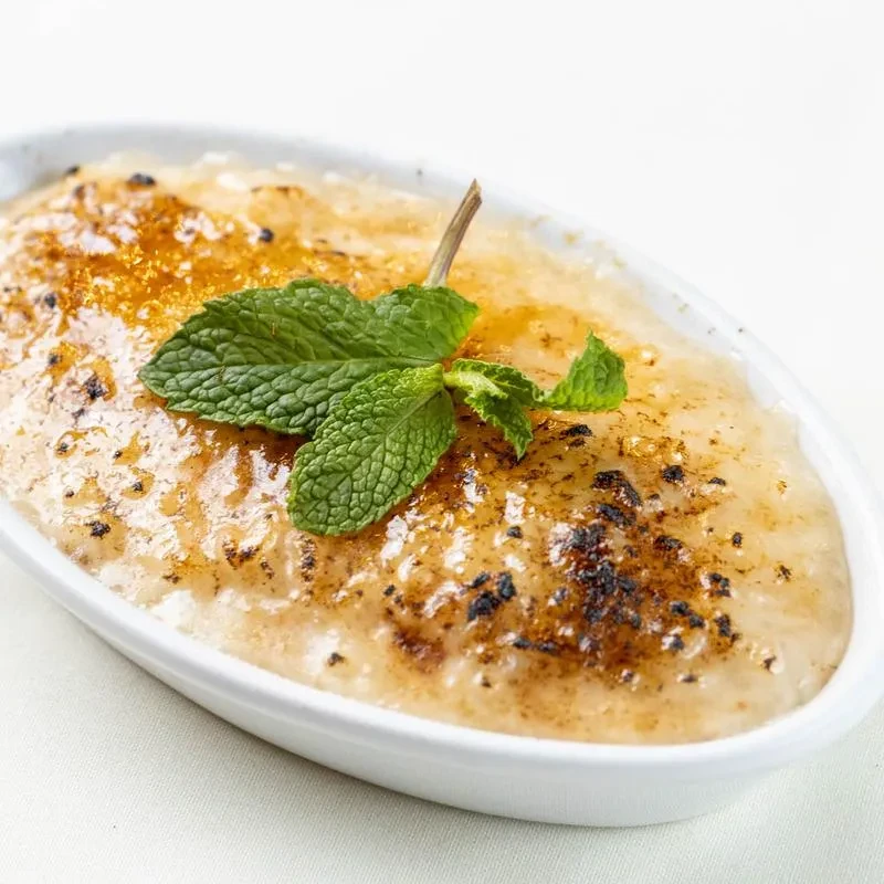 An oval dish of creme brulee with toasted sugar and mint leaves.