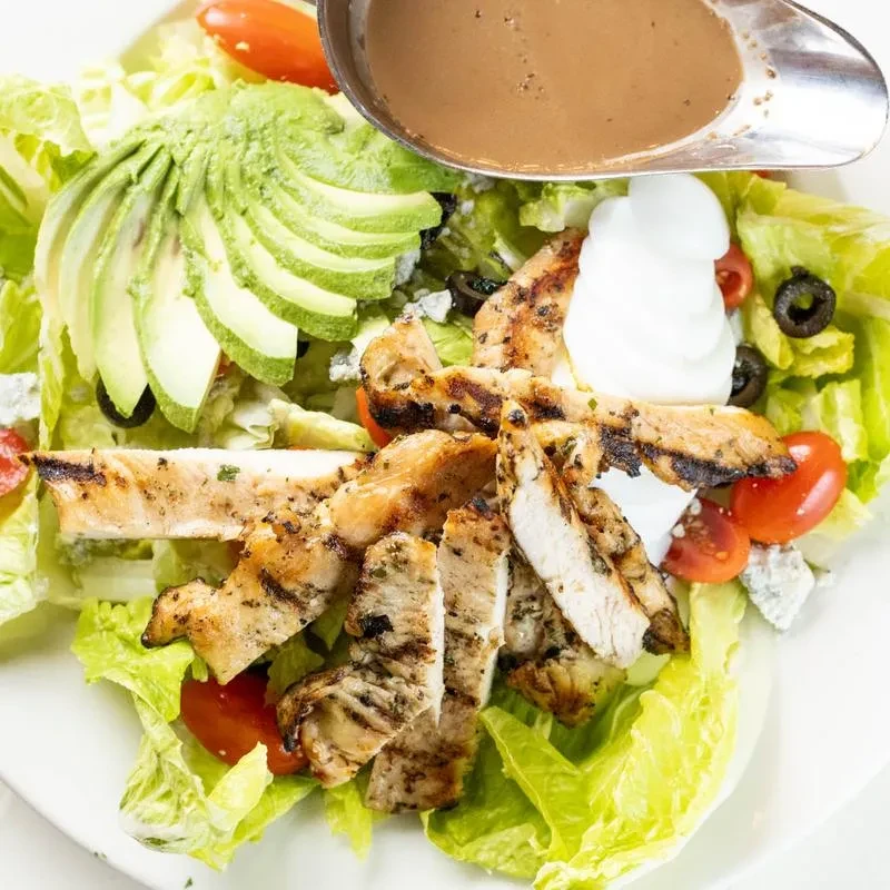 Grilled chicken salad with avocado, tomatoes, olives, and dressing.