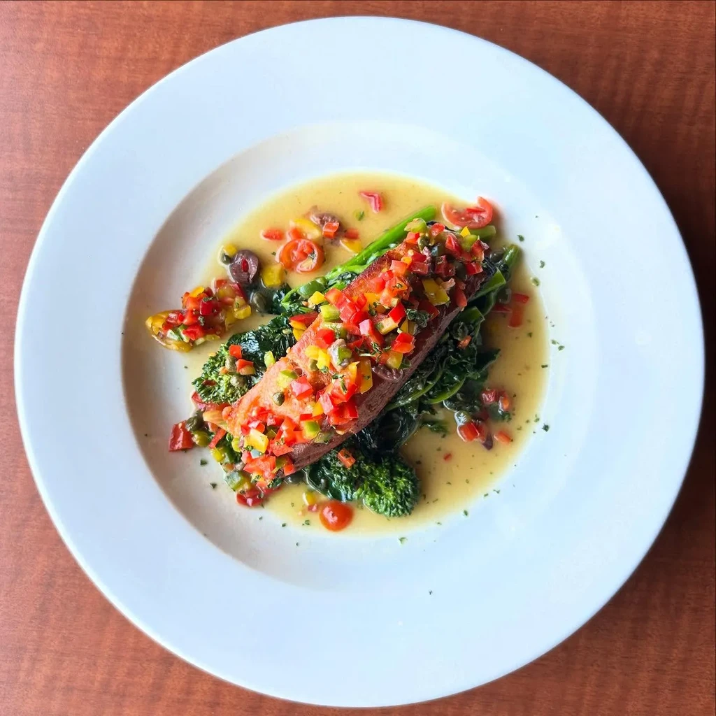 Salmon fillet with diced bell peppers, broccoli rabe, and sauce.