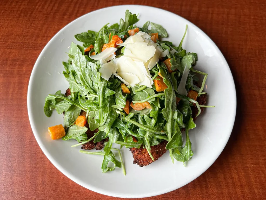 Breaded cutlets topped with arugula, roasted squash, and shaved cheese.