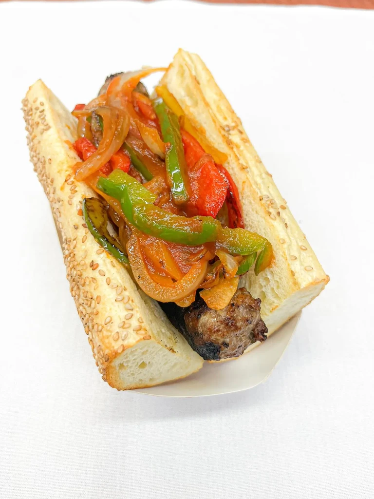 Sausage sandwich with sautéed peppers and onions on a sesame seed roll.