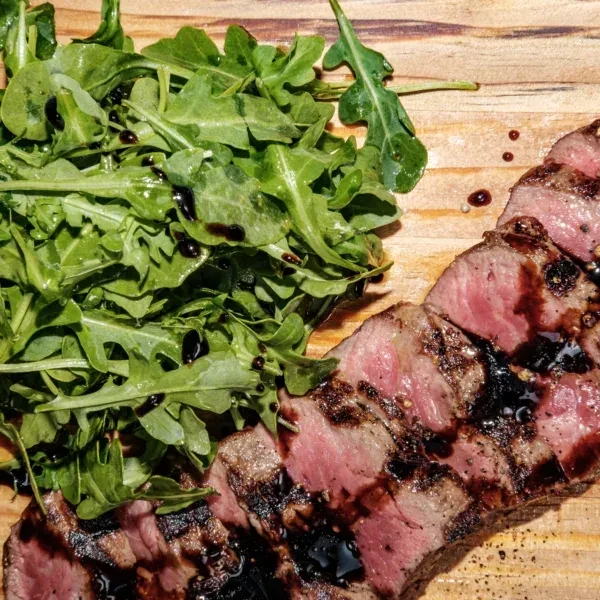 Sliced steak with balsamic glaze and a side of arugula.