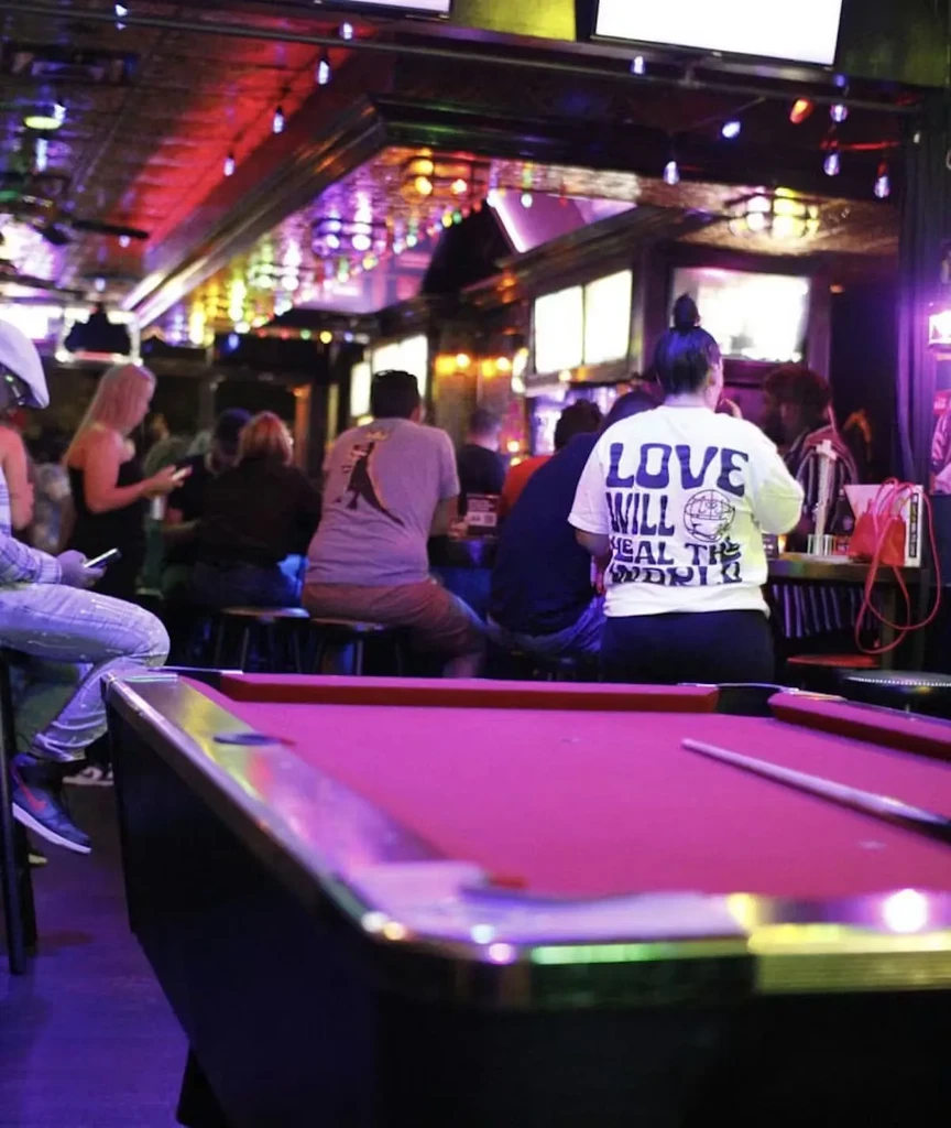 Vibrant magenta pool table inside a dimly lit, colorful bar.