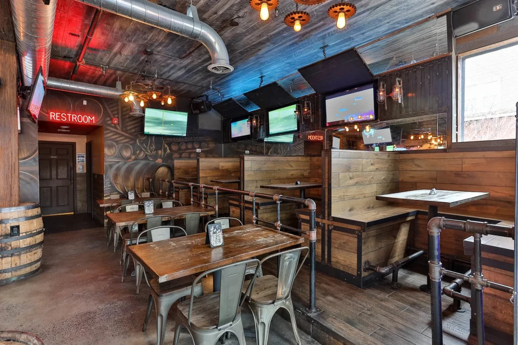 An empty industrial-style restaurant interior with wooden tables and metal chairs.