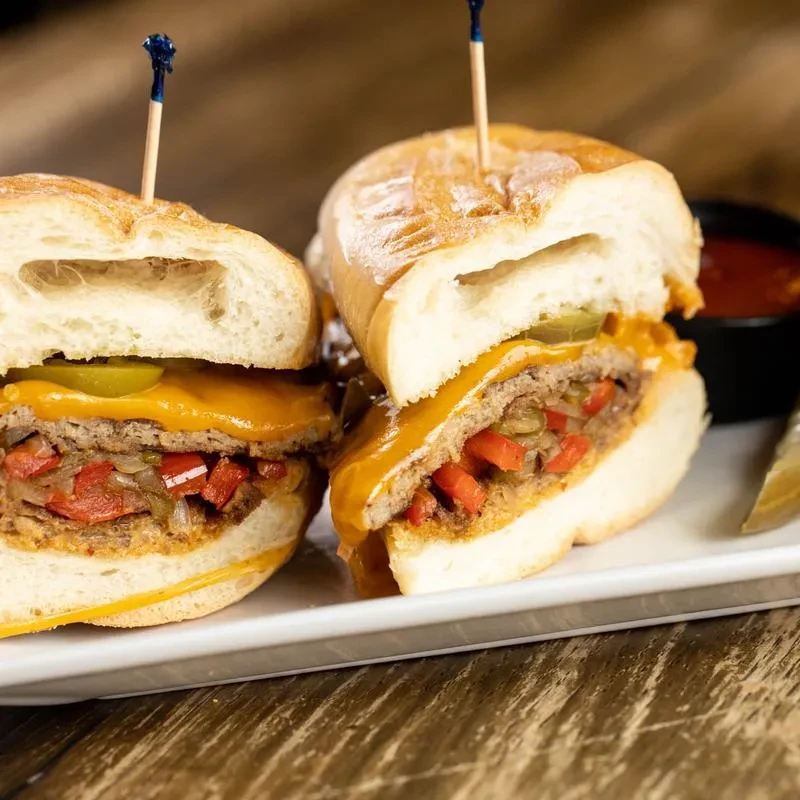 Two cheeseburger sliders with peppers, onions, and pickles on a white plate.