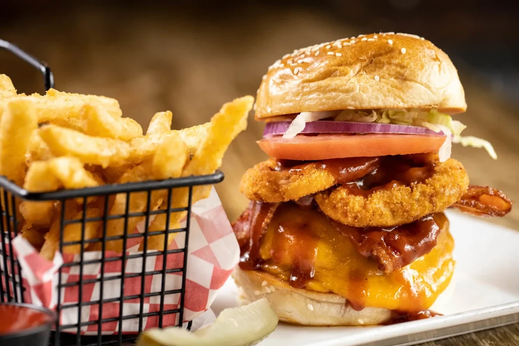 Cheeseburger with onion rings, bacon, BBQ sauce, and a side of fries.
