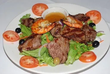 A plate of steak and shrimp salad with tomatoes, olives, and dressing.