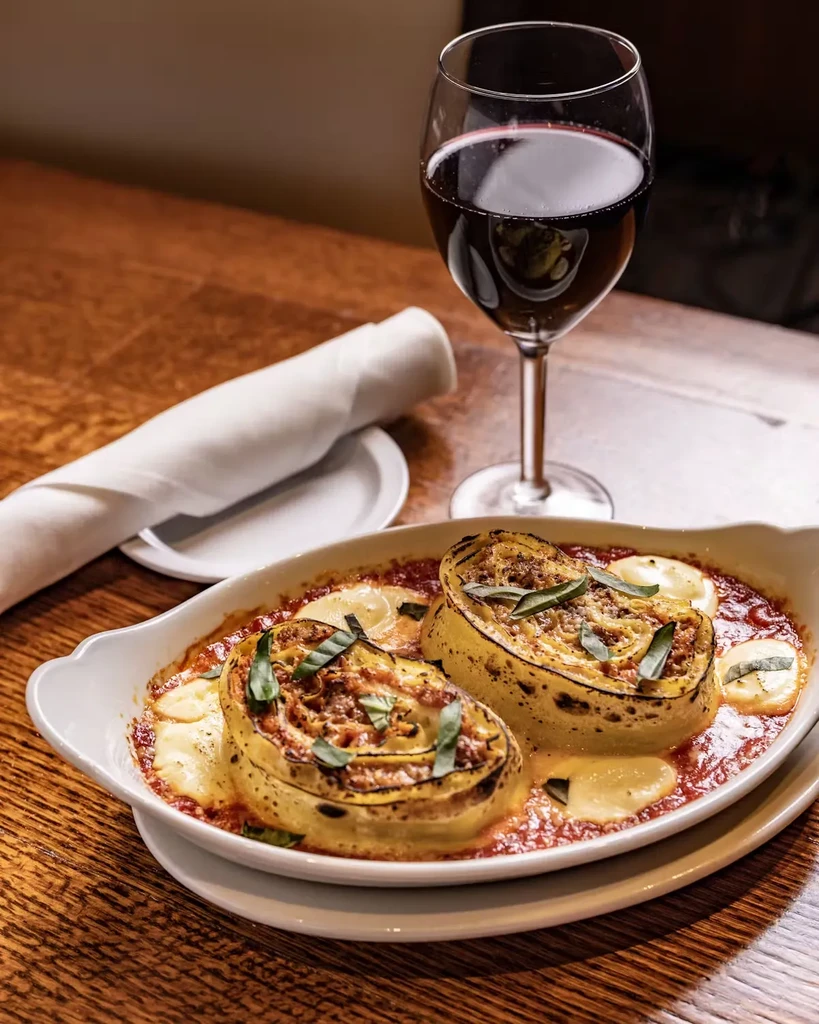 Two pasta rolls in tomato sauce with mozzarella and basil, next to red wine.