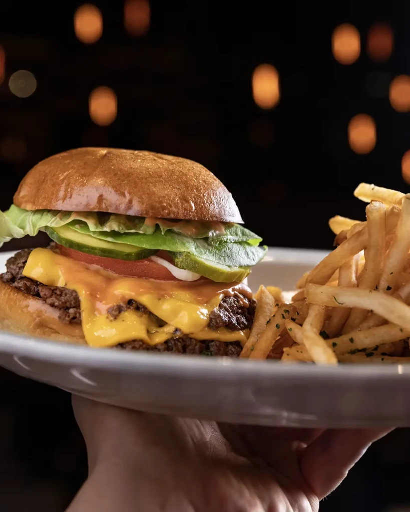 A hand holds a plate with a cheeseburger and french fries.
