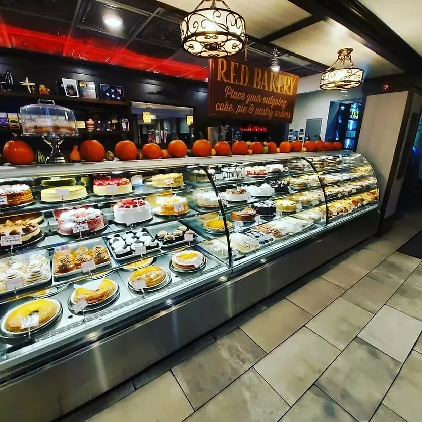A bakery display case full of cakes and pastries, with pumpkins on top.