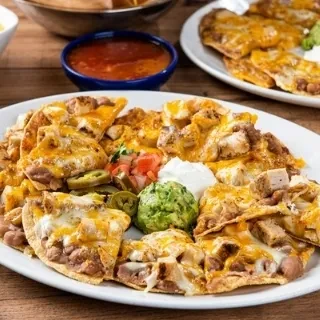 A large plate of chicken nachos with guacamole, sour cream, and salsa.