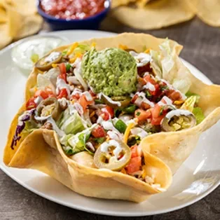 A taco salad in a crispy tortilla bowl with salsa and chips.