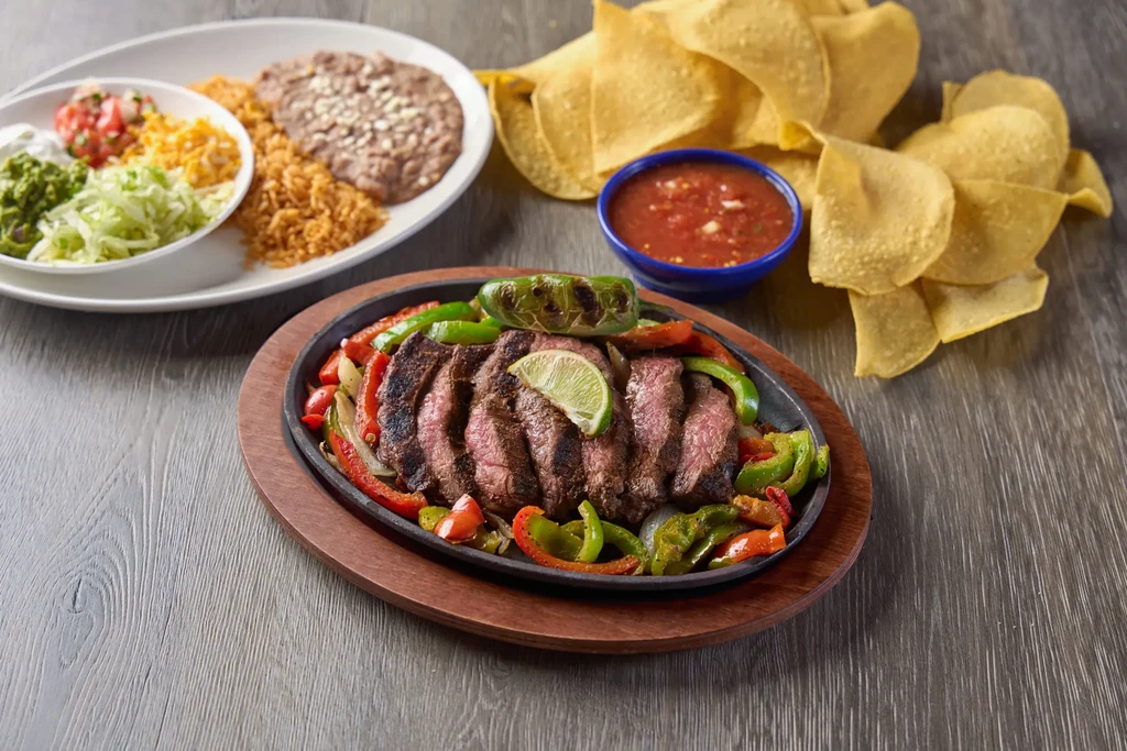 Steak fajitas, rice, beans, toppings, salsa, and tortilla chips.