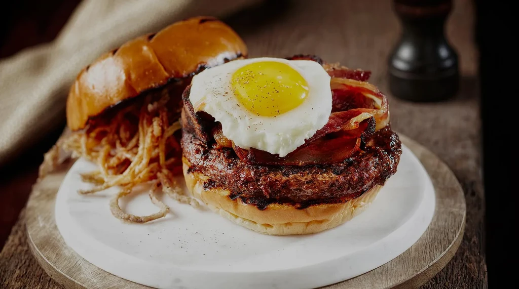 An open-faced burger with bacon, a fried egg, and crispy onions.