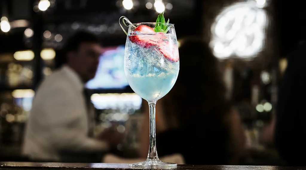 A blue cocktail with strawberry and mint garnish on a bar.