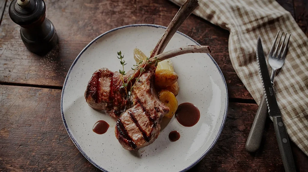 Grilled lamb chops with potatoes, sauce, and thyme on a white plate.