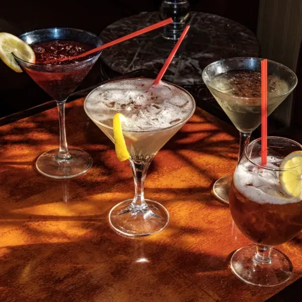 Four cocktails in various glasses with red straws and lemon garnishes.