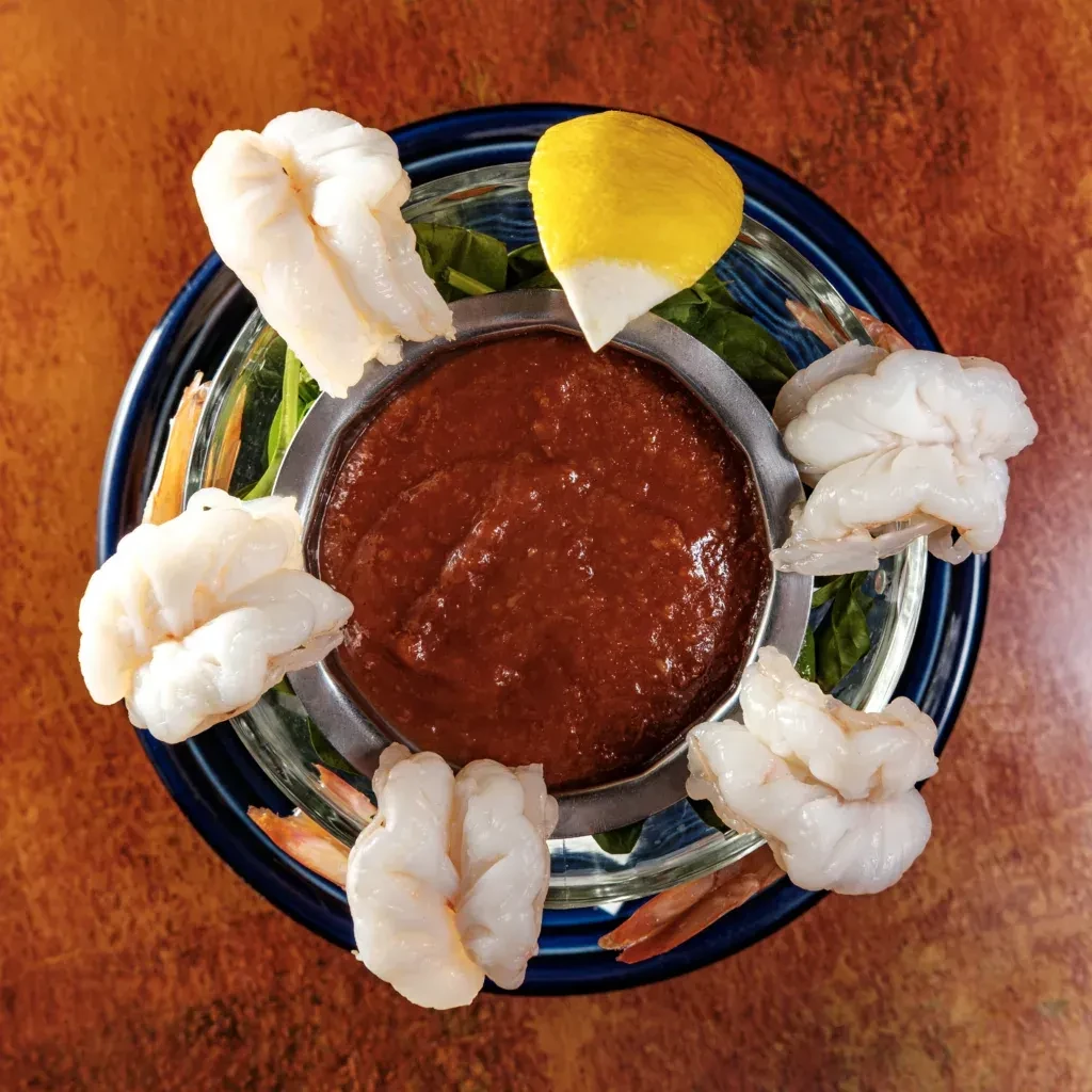 Shrimp cocktail with sauce and lemon wedge, overhead view.
