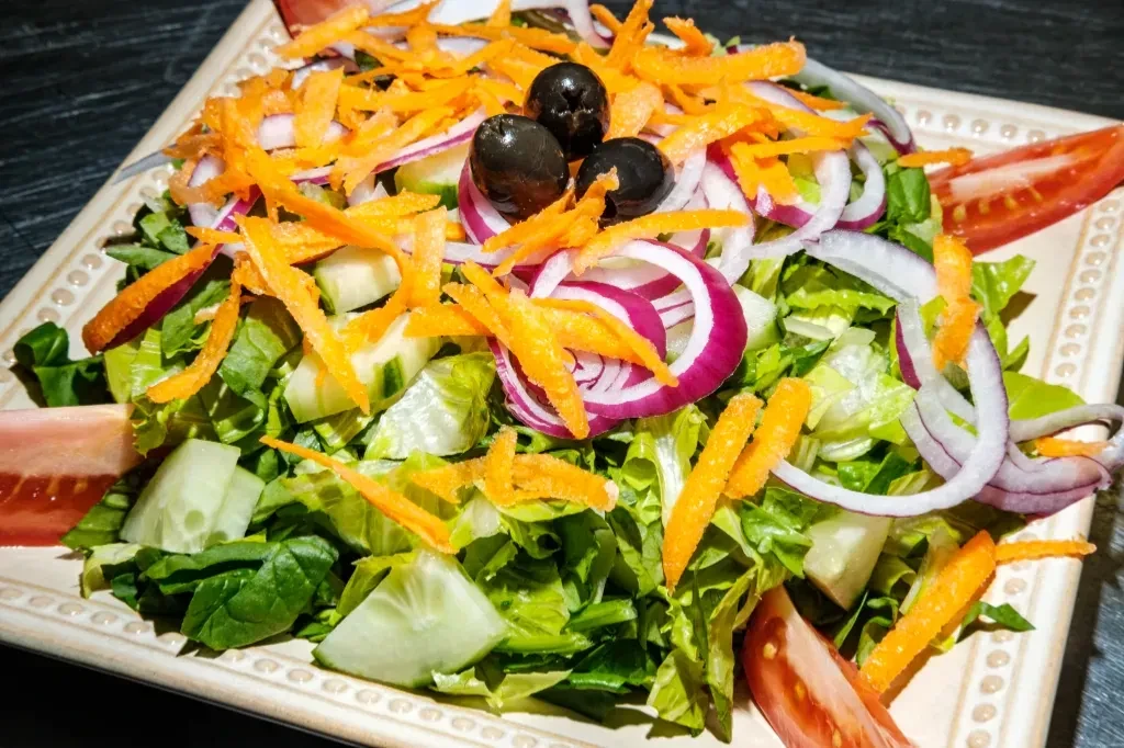 A fresh salad with lettuce, carrots, onions, cucumbers, tomatoes, and olives.