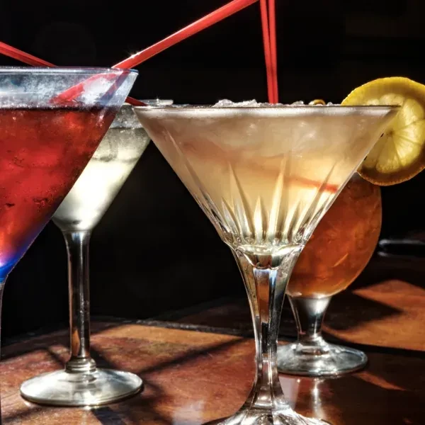 Four different cocktails with red straws on a dark table.