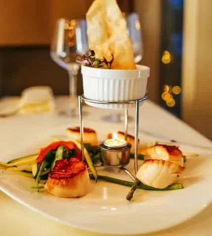 Seared scallops with vegetables, a dip, and a candle on a white plate.