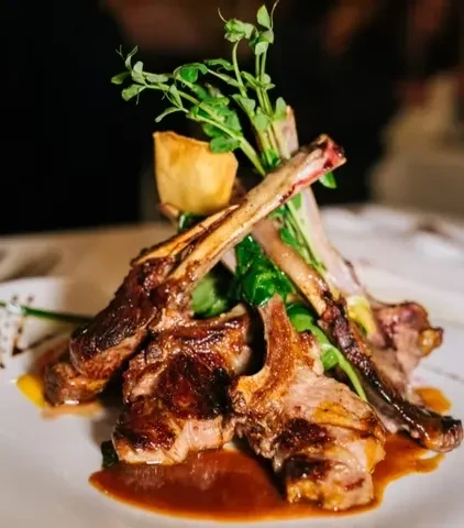 Grilled lamb chops with greens, a yorkshire pudding, and sauce.