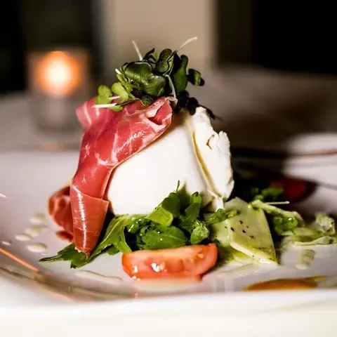 A burrata dish with prosciutto, arugula, and tomato.