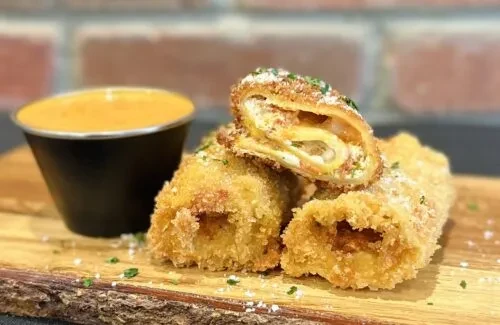 Deep-fried rolls with sauce on a wooden board.