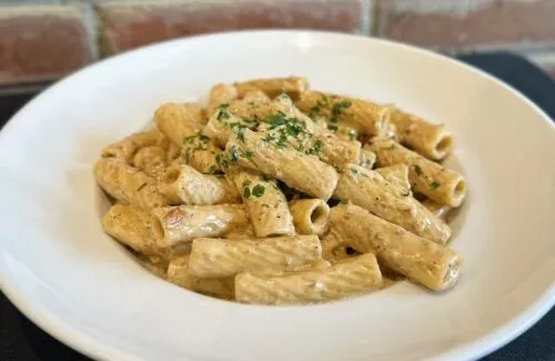 A close-up of rigatoni pasta with a creamy sauce and parsley.