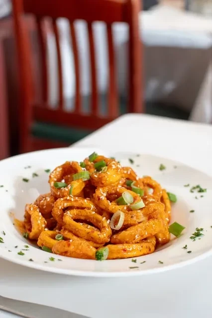 A white bowl of crispy calamari, topped with sesame seeds and green onions.