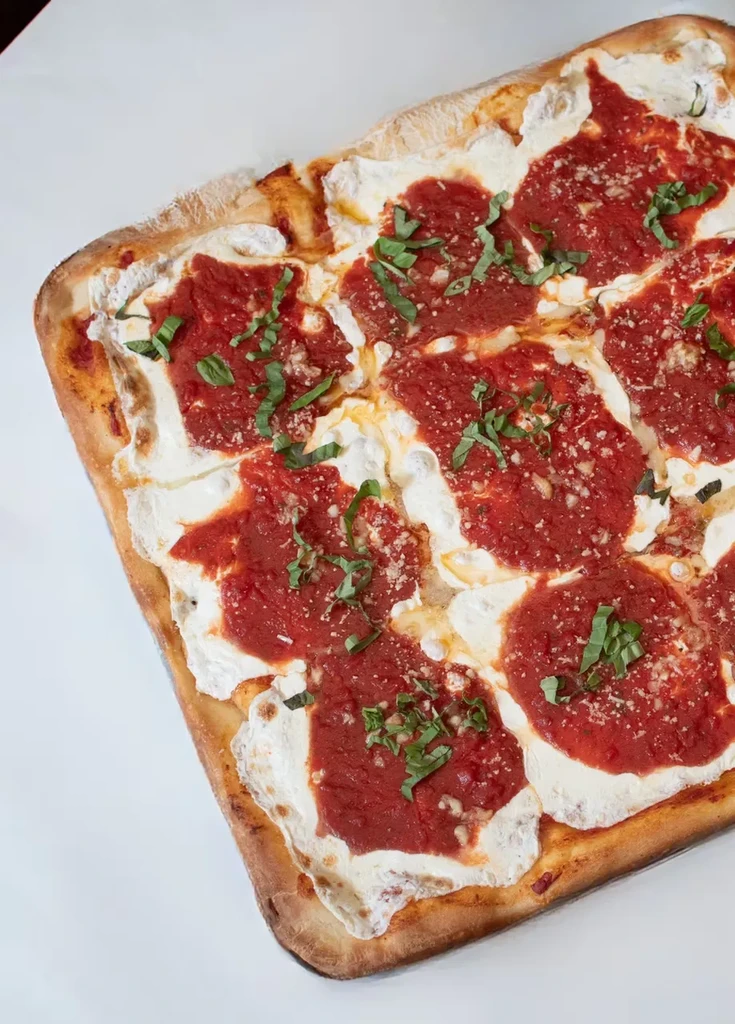 A rectangular pizza with red sauce, white cheese, and green basil.