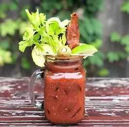 Bloody Mary in a mason jar garnished with celery, olive, lime, bacon.
