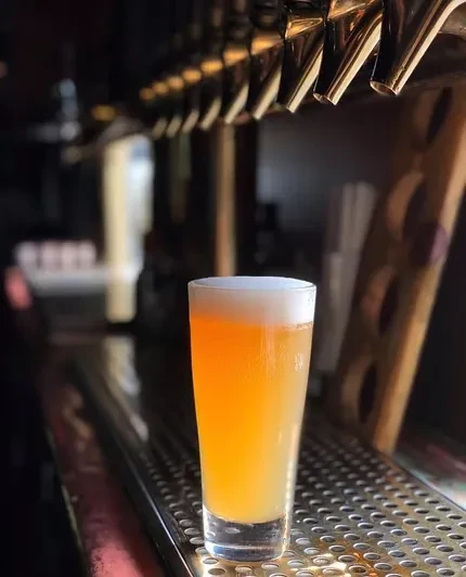 A tall glass of beer with foam on a bar counter.