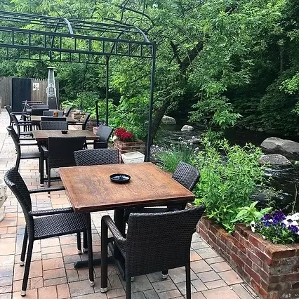 An outdoor restaurant patio with tables, chairs, and a river nearby.