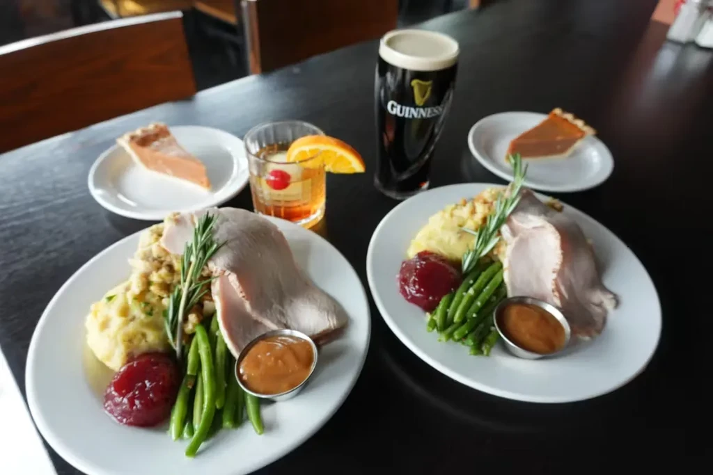 Two Thanksgiving dinners with pie, old-fashioned cocktails, and Guinness on a table.