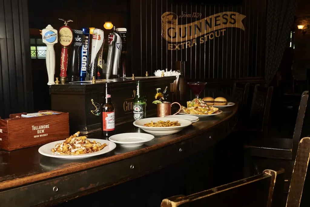 A dark, long bar with draft beer taps, bottles, and food plates.