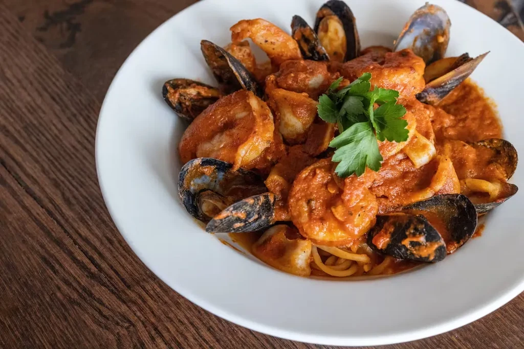 White bowl of spaghetti with mussels, shrimp, and tomato sauce.