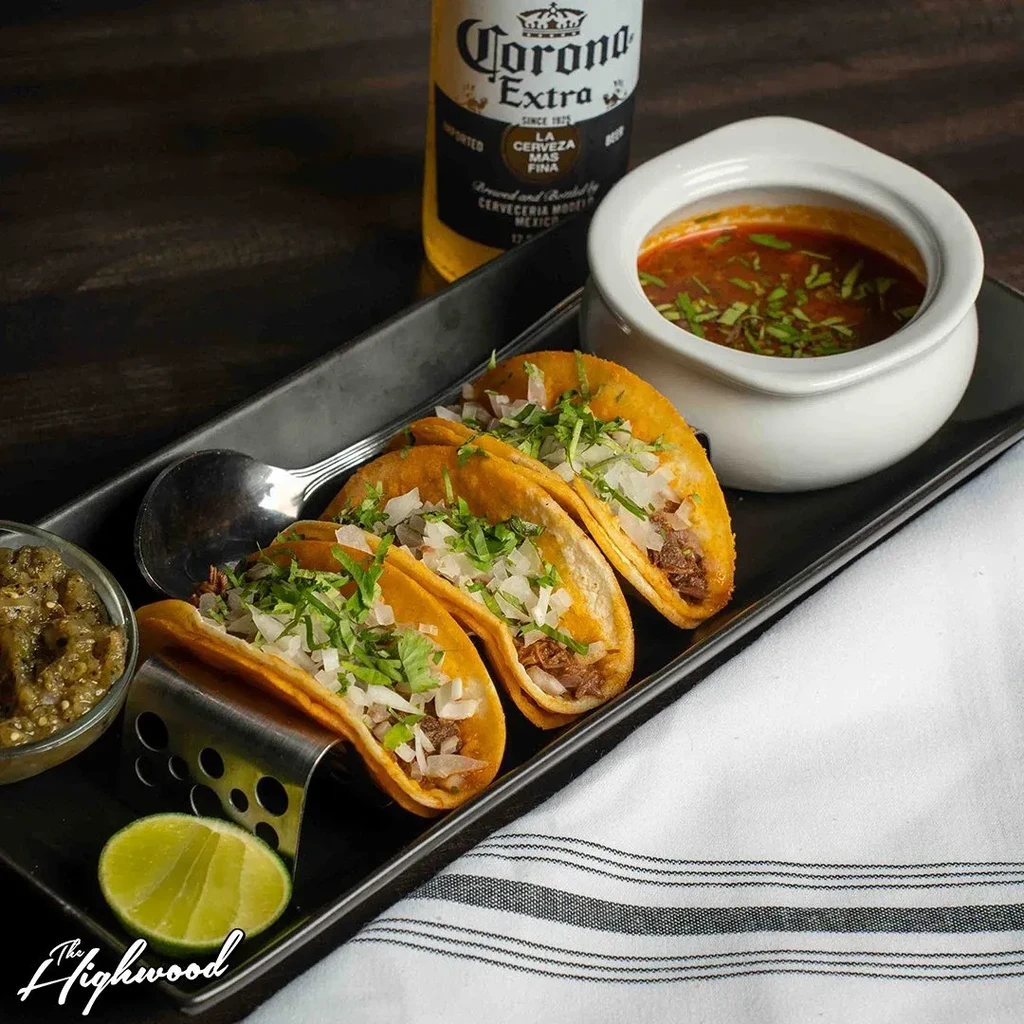 Three tacos, a bowl of soup, lime, and beer on a tray.