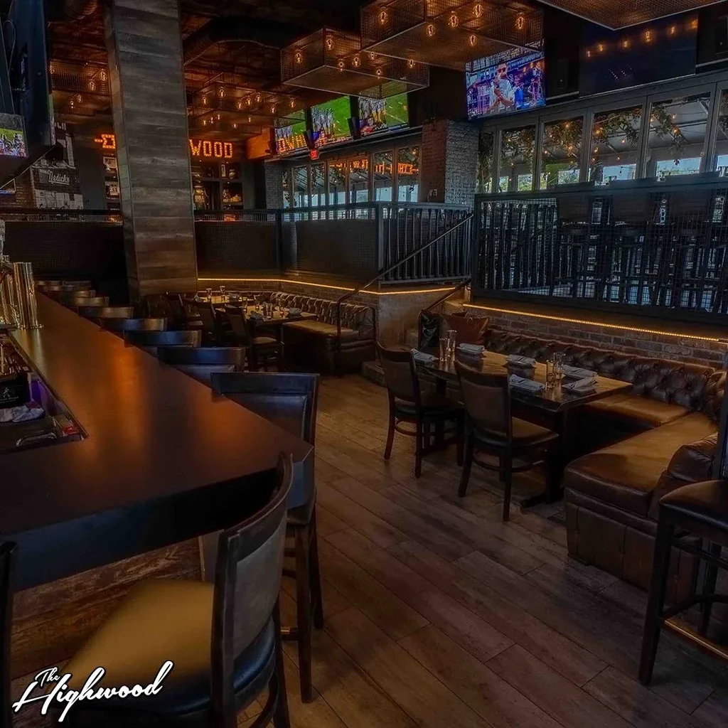 An upscale restaurant with a long bar, dining tables, and large TVs.