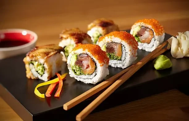 Sushi rolls on a black platter with chopsticks, wasabi, and soy sauce.