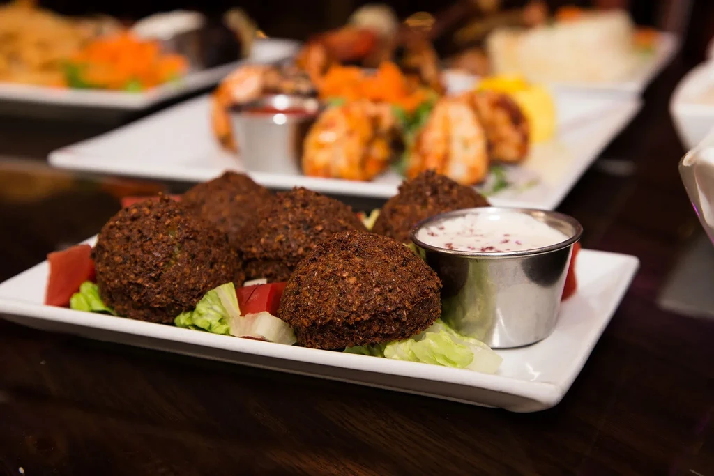 Falafel, lettuce, tomatoes, and dipping sauce on a white plate.