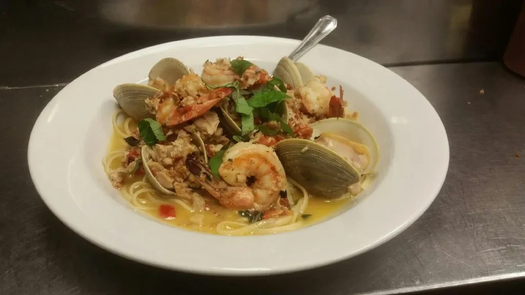 Seafood pasta with shrimp, clams, and herbs in a white bowl.