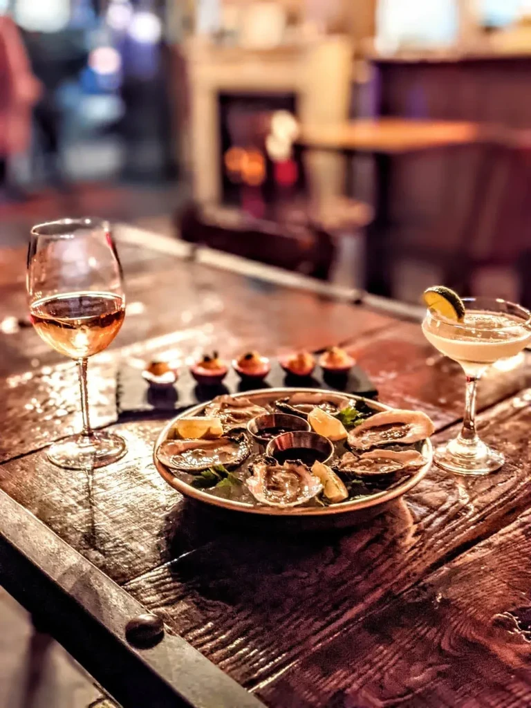 Oysters, rose wine, and a cocktail on a wooden table.