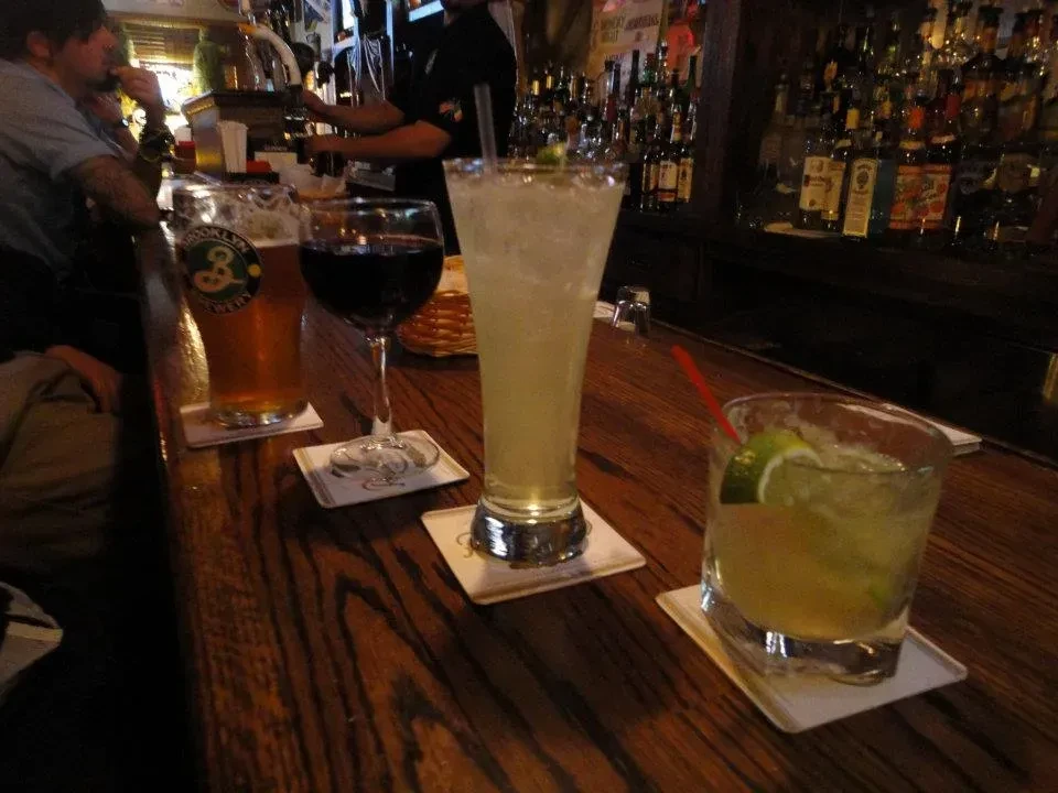Three drinks, beer, wine, and a cocktail, on a bar counter.