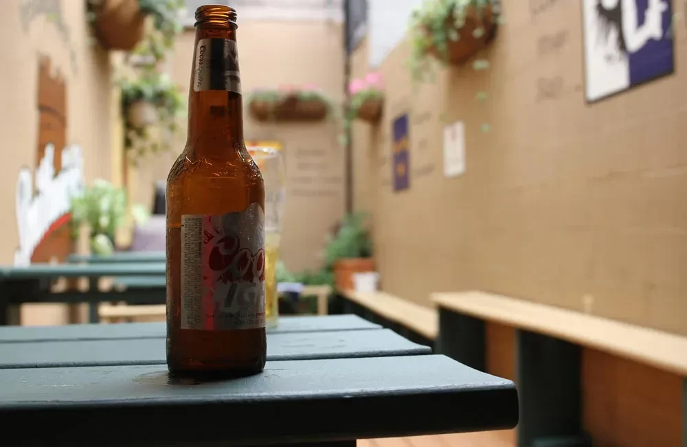 A sweating bottle of Coors beer on a dark green table.