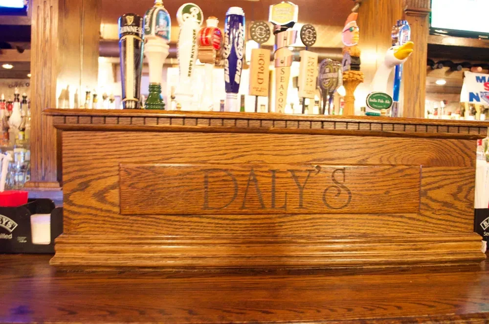 A wooden bar with "DALY'S" carved into it, featuring many beer taps.